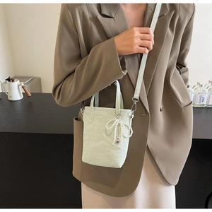 Detail of mint green pleated bucket bag with pearl bow charm worn on brown blazer