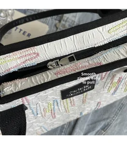 Close-up of the smooth silver zipper and colorful embroidery on the white textured tote bag