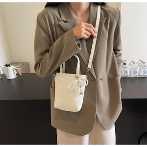 Detailed view of a white bucket bag with pearl bow charm and heart pendant accessory