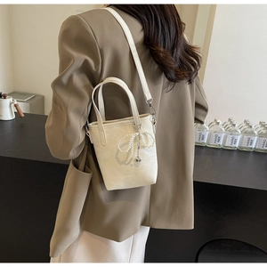 Detail of cream bucket bag with pearl bow charm and adjustable shoulder strap