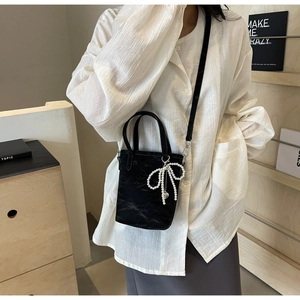 Detailed view of black pleated tote bag with pearl bow charm and logo detail
