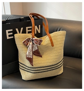 Detail of straw tote bag with brown leather handles and bear scarf on leather sofa