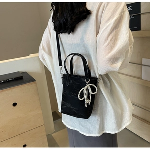 Detail of black nylon bucket bag with ruffled texture and white pearl bow charm accent