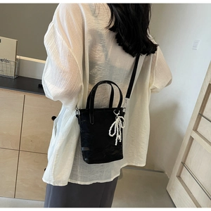 Detail of a black bucket bag featuring a pearl bow charm and leather handle