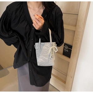 Silver bucket bag with pleated texture and pearl bow charm shown in lifestyle setting
