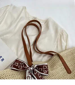 Detail of hand-woven straw shoulder bag featuring brown leather straps and silk scarf accent
