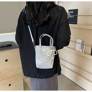 Silver pleated bucket bag with pearl bow charm shown as a stylish crossbody on a model