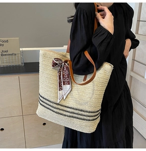 Close-up of beige straw tote bag with black stripes, leather straps, and patterned scarf