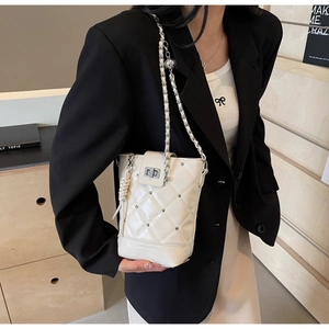 Detail einer cremeweißen Steppmuster-Beuteltasche mit Nieten und Kettenriemen