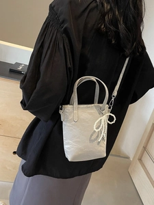 Gray pleated bucket bag with pearl bow charm shown as a stylish crossbody on a model