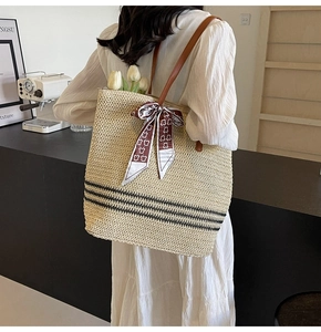 Détail d'un sac cabas en paille tissée avec lanières en cuir marron et rayures sur fond noir