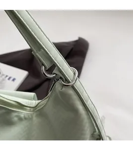 Gros plan sur la bandoulière en cuir vert clair et les anneaux en métal de ce sac fourre-tout