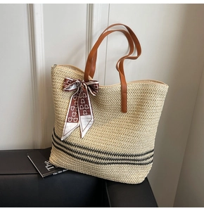 Détail du sac cabas en paille tressée avec rayures noires et lanières en cuir brun