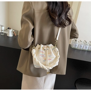 Detail of white canvas bucket bag with rainbow stitching and woven handle on a table