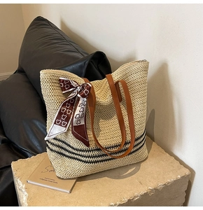 Détail du sac cabas en paille tissée avec anses en cuir et foulard sur socle en pierre
