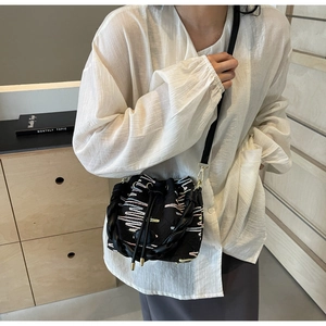 Detail of black drawstring bucket bag featuring colorful wave embroidery and woven handle