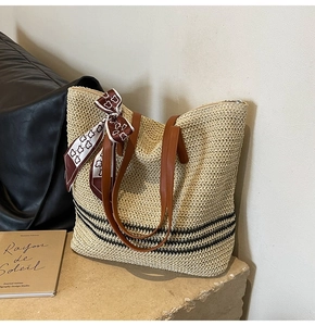 Detailed close-up of straw woven tote bag with black stripes and brown leather handles