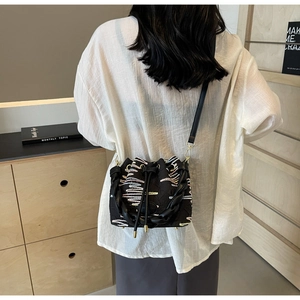 Detail of black canvas bucket bag featuring colorful wave embroidery and braided handle