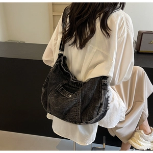 Rear view of a black washed denim hobo bag with adjustable wide strap on model