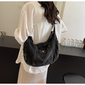 Detailed view of washed black denim hobo bag featuring a front pocket and frayed edges