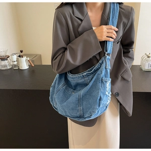 Detailed close-up of blue denim crossbody bag featuring distressed fabric and wide strap