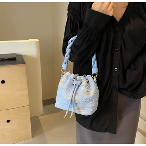 Close-up of light blue textured bucket bag with embroidered patterns and woven handle