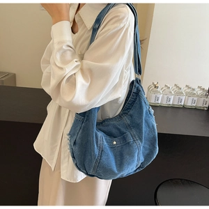 Detail of blue denim hobo bag featuring raw edges and a front pocket with metal button