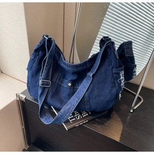 Detail of dark blue denim tote with adjustable strap, metal buckle, and frayed edge design