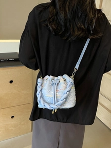 Light blue canvas bucket bag with woven handle and colorful embroidery in a crossbody view