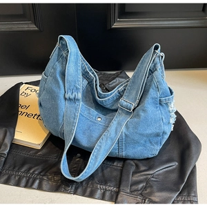 Detail of the adjustable wide shoulder strap and raw frayed edges on the denim hobo bag