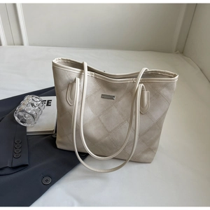 Detailed view of beige tote bag with diamond quilted pattern and silver metal logo plate