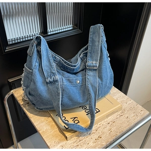 Detail of blue denim hobo bag featuring vintage frayed tassels and adjustable strap
