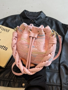 Pink drawstring bucket bag with woven handle and textured fabric on leather background