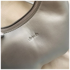 Macro detail of silver pleated cloud bag showing lychee leather texture and branding