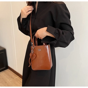 Sac bandoulière en cuir huilé marron avec logo blanc et pendentif en forme de cœur