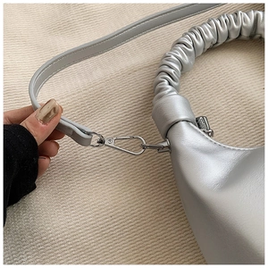 Detail of silver metallic handbag featuring ruched cloud handle and detachable strap