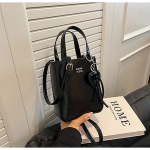 Détail d'un mini sac cabas en cuir verni noir avec breloque cœur et lettrage blanc