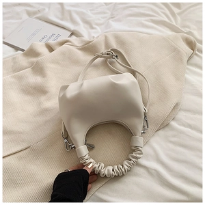 Detail of cream pleated handle and smooth PU leather surface on moon shaped crossbody bag