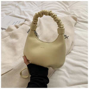 Detail of creamy yellow crescent bag with scrunchie handle and logo on leather surface