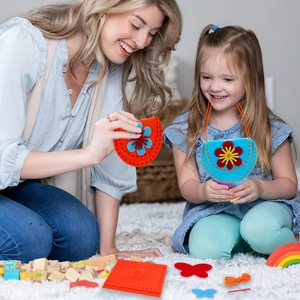 Mother and daughter making colorful DIY felt handbag sewing kit for kids on white rug