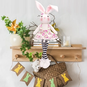 Detail of fabric Easter bunny doll with pink floral dress and striped legs on shelf