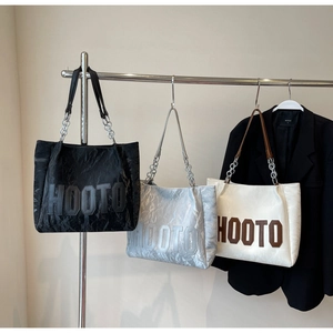 Close-up of pleated tote bags in black, silver, and cream with metallic chain straps