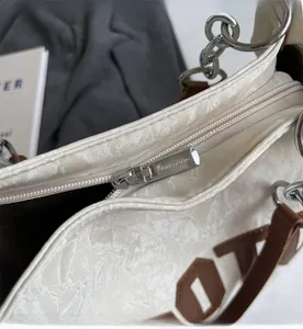 Detailed close-up of smooth silver zipper and metal chain on a beige tote bag