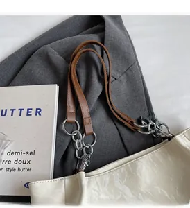 Detail of off-white tote bag with silver metal chain handle and textured fabric finish