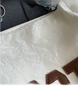Detail of creamy white crinkled leather tote bag with brown letter patch and silver metal ring