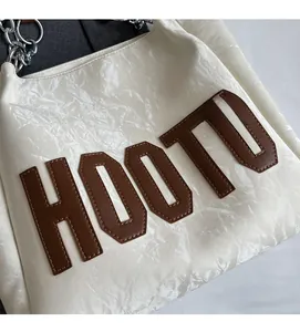 Detail of white wrinkled leather tote with brown HOOTU letter patches and silver chain strap