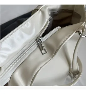 Close-up of smooth silver metal zipper on minimalist cream PU leather tote bag