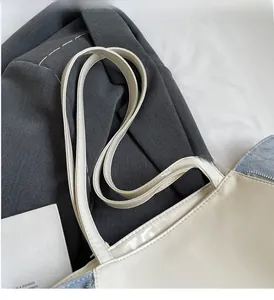 Detail of a color-block tote bag made from off-white PU leather and blue denim material