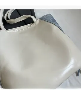 Detail of glossy beige tote bag featuring metal zipper closure and smooth leather texture
