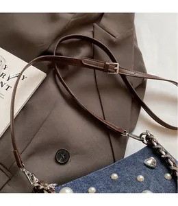 Détail du sac en jean avec perles, strass en cœur et bandoulière en cuir marron